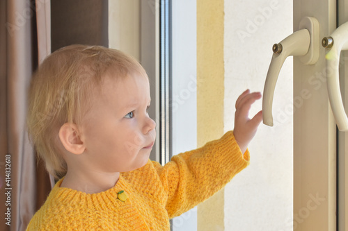 Baby the child sits at the window and looks at the lock of the window handle. Safety. Protective window limiters in the house. photo