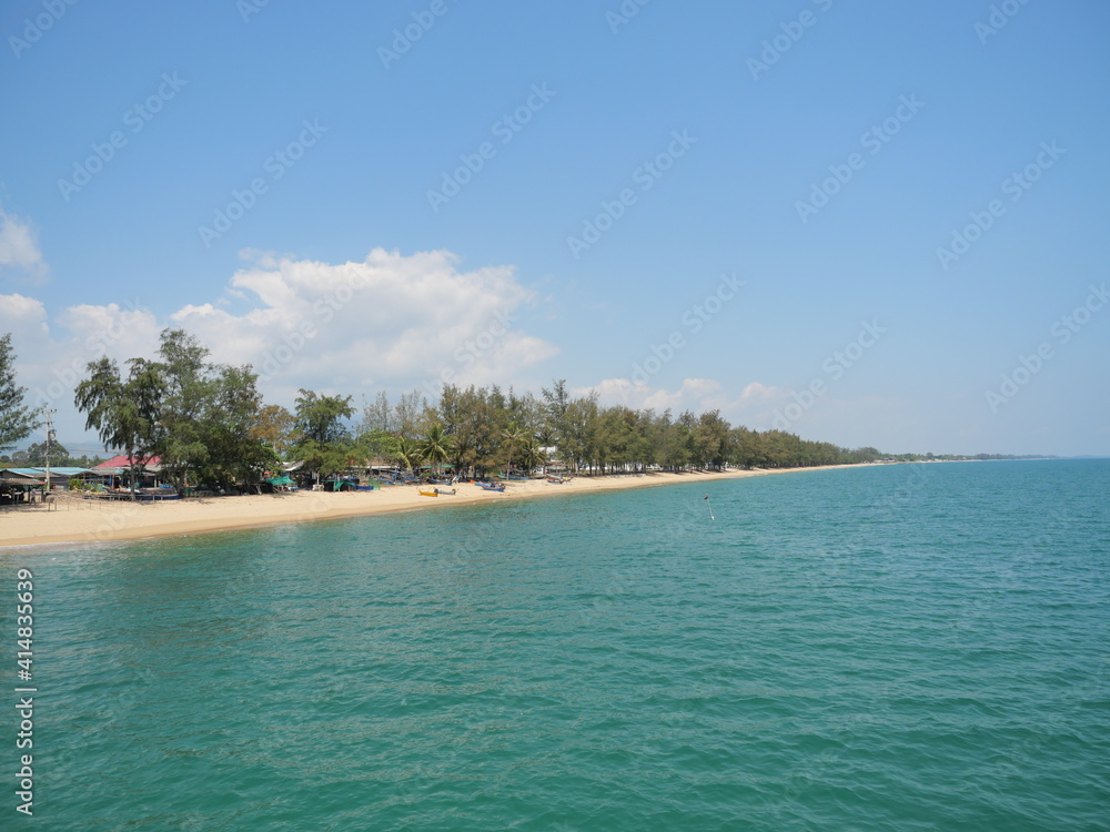 Green water in the sea with a fishing village on the brown sand beach with blue sky and white cloud in background, Prachuap Khiri Khan, Thailand	