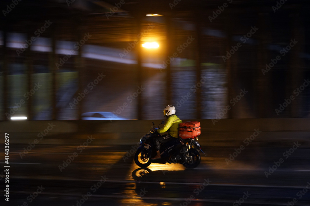 Panning shot of Shopee rider riding on a motorcycle with orange luggage box.
