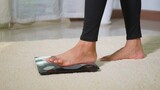 Asian young woman leg stepping standing on floor electric scales, female working out at home in living room, female stand on digital weighing machine. Healthy weight loss control concept, slow motion