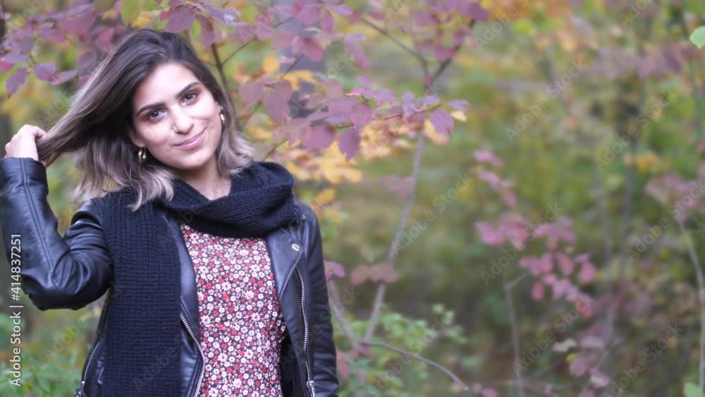 Brunette girl in autumn forest stands near yellow and red leafs and smiles in the camera Brunette girl in autumn forest stands near yellow and red leafs and smiles in the camera