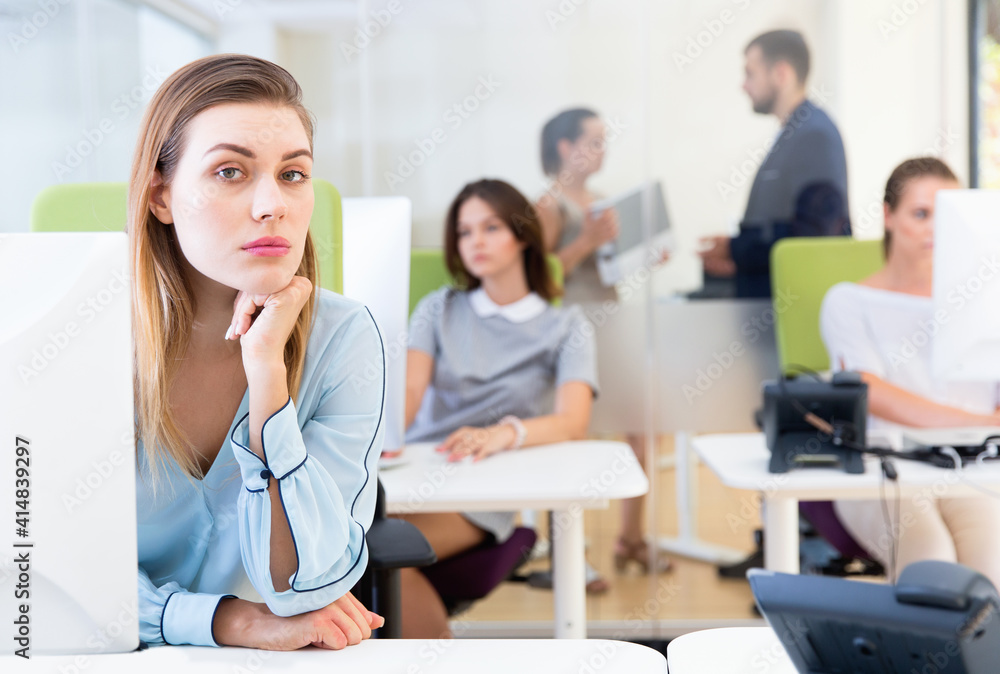Fototapeta premium Portrait of frustrated young unhappy business woman in coworking space with working colleagues behind