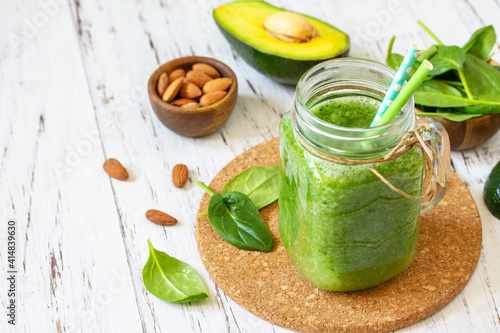 Healthy diet and nutrition, vegan, alkaline, vegetarian concepts. Green smoothie with spinach, avocado and almond nuts on a white wooden table. Copy space.