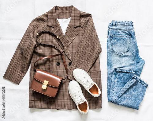 Women's clothing set - plaid jacket, mom's blue jeans, brown crossbody bag and sneakers on a light background, top view