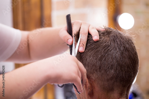 Male hairdresser, grooming men. Haircut styler and trimmer. The master cuts a man, shaves his temples and neck. The client at the hairdresser looks in the mirror. barbershop