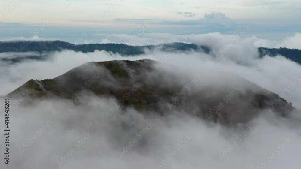 Slow aerial shot of thick fog clouds surrounding a Batur mountain in a tropical climate on the island of Bali Slow aerial shot of thick fog clouds surrounding a Batur mountain in a tropical climate on the island of Bali