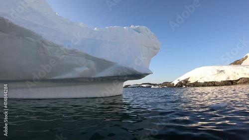 Wallpaper Mural A shot of a rowboat swimming a lap around a large iceberg lodged between two rocky seashores. The water is emerald green and the sky is blue, the sun shining bright over the Antarctic landscape. Torontodigital.ca