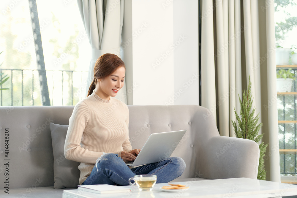 Fototapeta premium Young woman relaxing and drinking cup of hot coffee or tea using laptop computer
