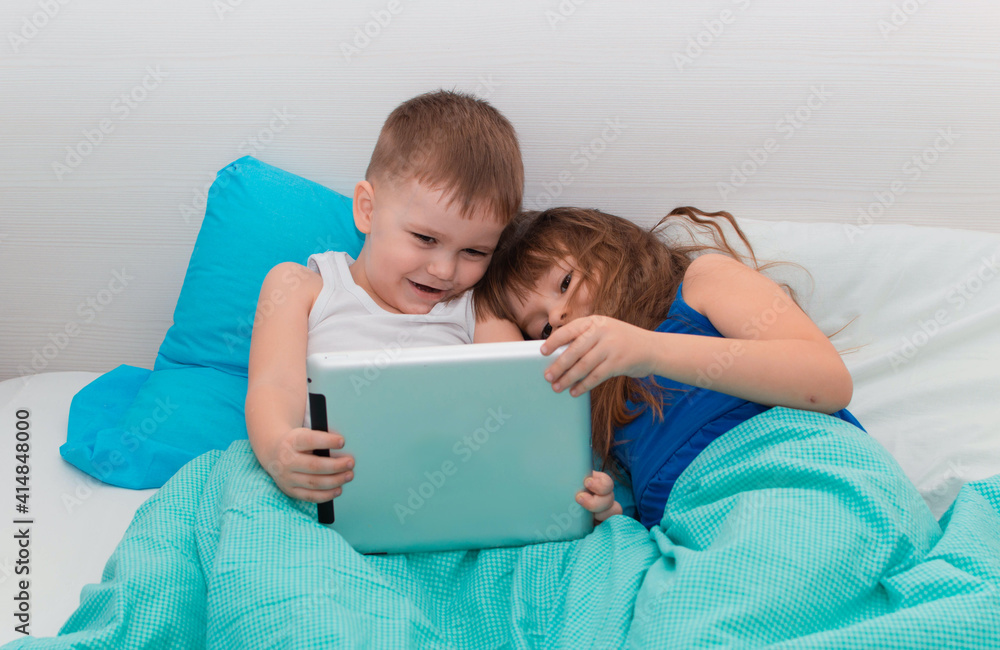 Young children enjoy digital gadget in bedroom of house. Children lie on bed and play on tablet. Education technology of learning concept of leisure. A child with gadget Young children enjoy digital gadget in bedroom of house. Children lie on bed and play on tablet. Education technology of learning concept of leisure. A child with gadget