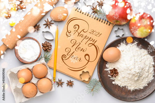 New Year composition with notebook and ingredients for preparing cookies on white background
