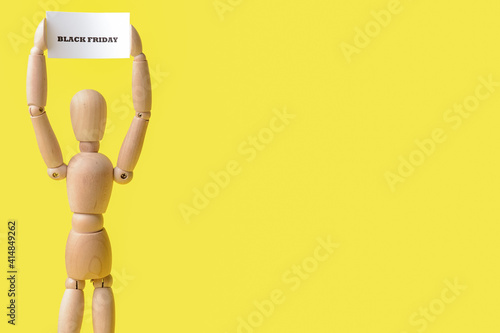 Wooden mannequin and card with text BLACK FRIDAY on color background