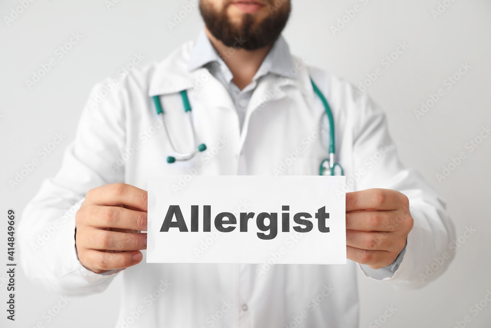 Doctor holding paper with word ALLERGIST on light background Doctor holding paper with word ALLERGIST on light background