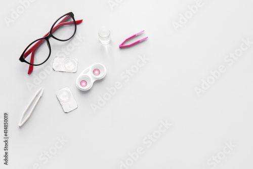 Eyeglasses, tweezers and container with contact lenses on light background