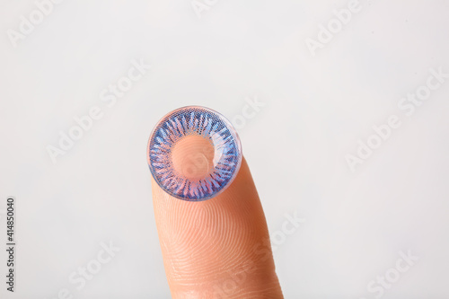 Female finger with contact lens on light background