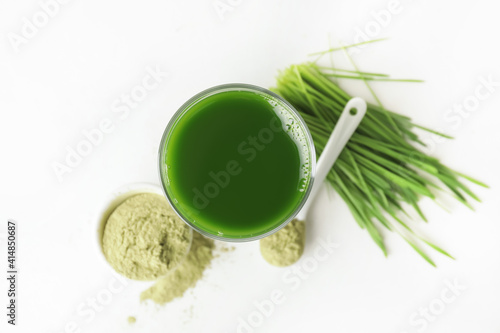 Glass with fresh wheatgrass juice and powder on white background photo