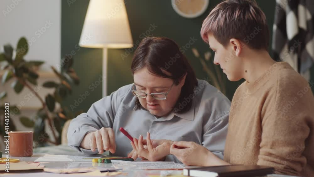 Adult Caucasian man with Down syndrome and female teacher drawing on paper during therapeutic art lesson at home Adult Caucasian man with Down syndrome and female teacher drawing on paper during therapeutic art lesson at home