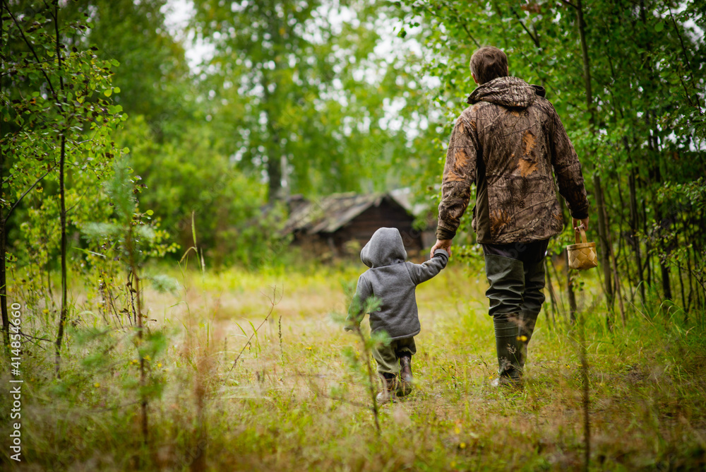 a small boy and an adult walk through the woods to a wooden house, selective focus