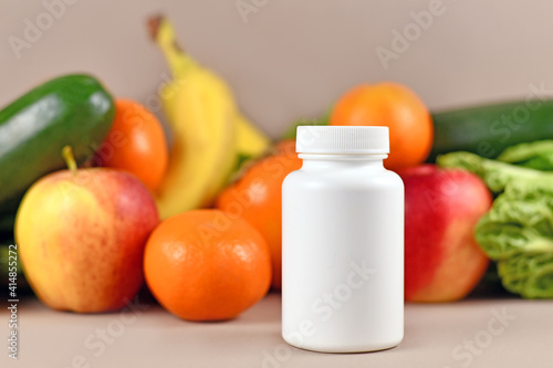 White food nutrition supplement bottle in front of fruits and vegetables in blurry background