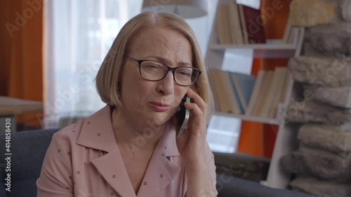 Blonde old lady who speaks furious on her cell phone at home gets angry. Concept of talking furious over the phone.