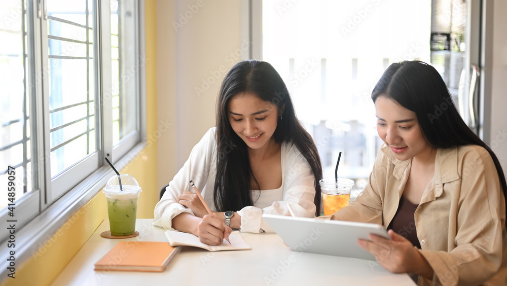 Two young woman using digital tablet and discussing their project at cafe.