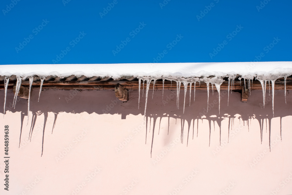 Very beautiful icicles hanging from the snow-covered roof. Icicles falling danger concept. Very beautiful icicles hanging from the snow-covered roof. Icicles falling danger concept.