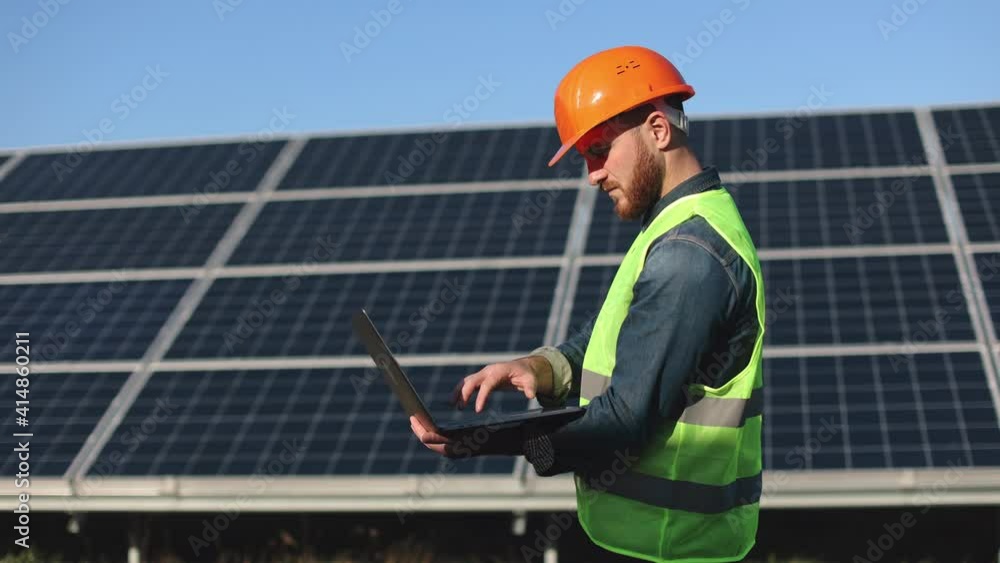 The engineer is entering the data into the laptop. He is standing next to solar panels. 4K. The engineer is entering the data into the laptop. He is standing next to solar panels. 4K.