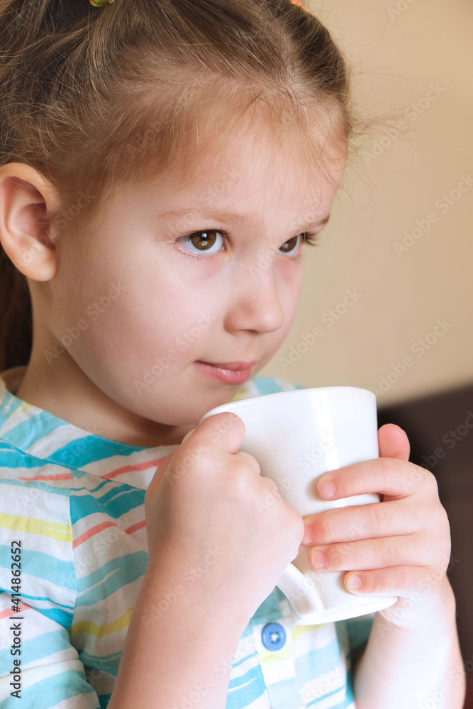 Little girl in morning in kitchen holding a mug in her hands, having breakfast, Relaxing with drink. Child drink beverage Little girl in morning in kitchen holding a mug in her hands, having breakfast, Relaxing with drink. Child drink beverage