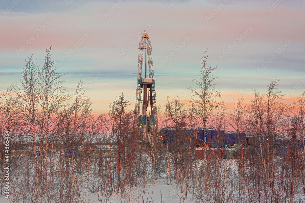 The landscape of the northern landscape of an oil and gas field with a drilling rig against the backdrop of a beautiful sky. Winter polar day