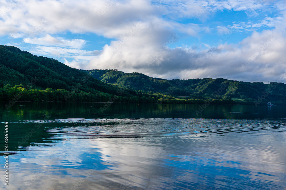 湖の湖面に反射する青い空と緑の山なみ
