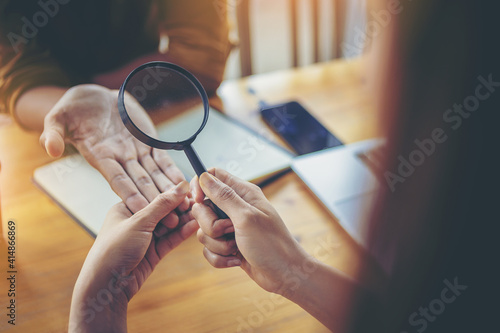 A woman seer is watching horoscope for her colleague. The young woman shining a magnifying glass to colleague in office. photo