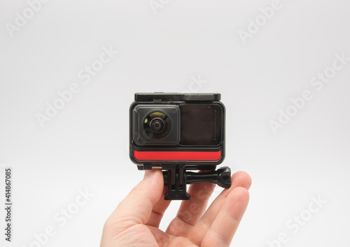 in the hands of a man modern panoramic action camera aimed at it, white background.