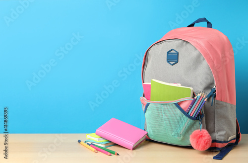 Stylish backpack and different school stationery on wooden table against light blue background, space for text. Back to school