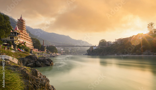 Obraz na płótnie Stunning view of the Ganga river embankment with the Lakshman Jhula bridge and Tera Manzil Temple (Trimbakeshwar) during a beautiful sunset. Rishikesh, Uttarakhand, India. w salonie