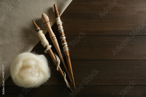 Soft white wool with spindles on wooden table, flat lay. Space for text