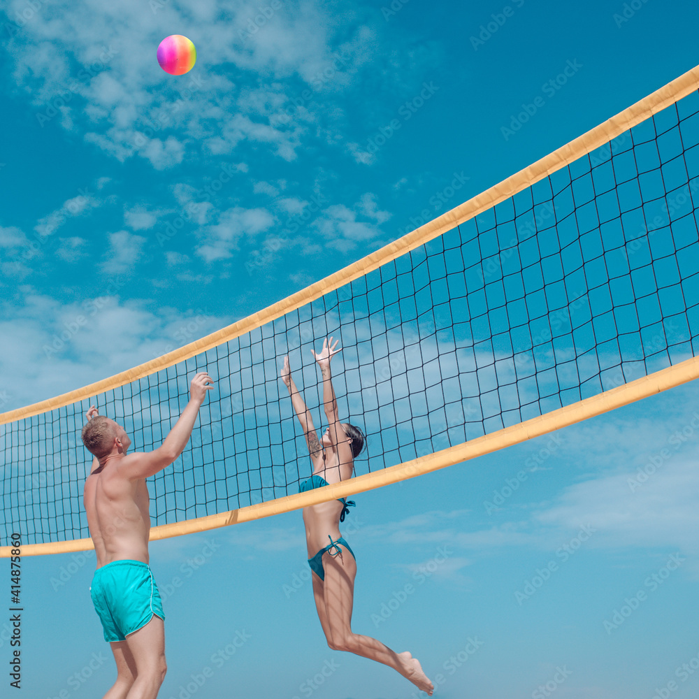 Couple in love play volleyball on sunny beach. Sexy woman and muscular man with ball at net. Love and flirting of couple. Sport activity and health