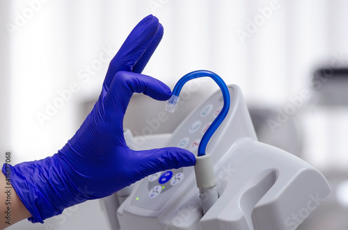 Saliva ejector and a hand in a disposable glove symbolize love in dentistry.Hand in a blue glove.Blue saliva ejector.The atmosphere of the dental office.With love in dentistry.Heart symbol.