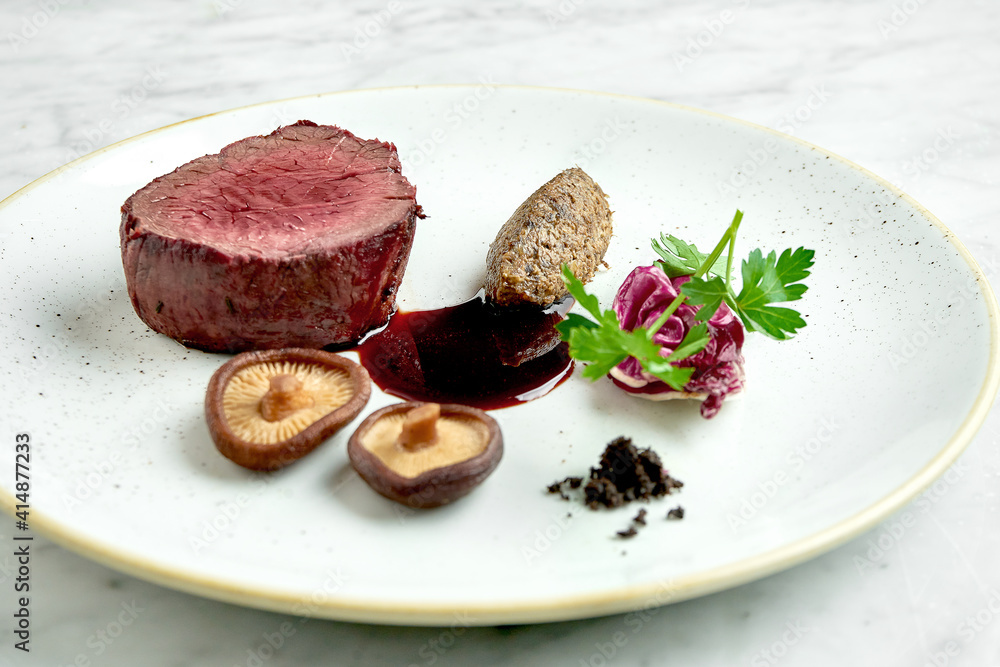 Appetizing medium rare beef steak with mushrooms and berry sauce, served in a white plate on a marble background. Restaurant food Appetizing medium rare beef steak with mushrooms and berry sauce, served in a white plate on a marble background. Restaurant food
