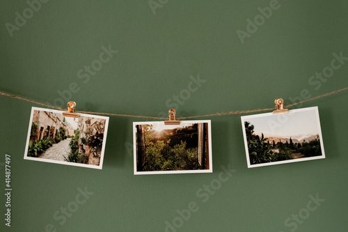 Postkarten mit Landschaftsmotiven an einer Schnur hängend vor einer grünen Wand, roséfarbene Klammern.