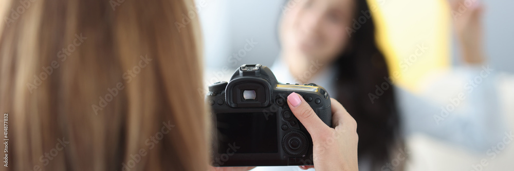 Black camera in hands of woman photographer with woman model on background in photo studio. Home photo session of friends tfc concept. Black camera in hands of woman photographer with woman model on background in photo studio. Home photo session of friends tfc concept.