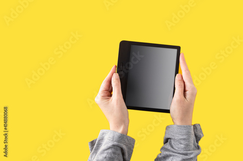 Hand wearing grey sweater and holding e-book reader on yellow panton background photo