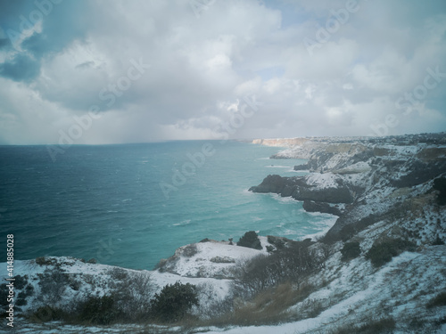 A snow storm covered the seashore. Bright turquoise sea, squally wind, huge waves, bright sun. The concept of bad weather, cold, sudden arrival of winter. Cape Fiolent Sevastopol Crimea top view