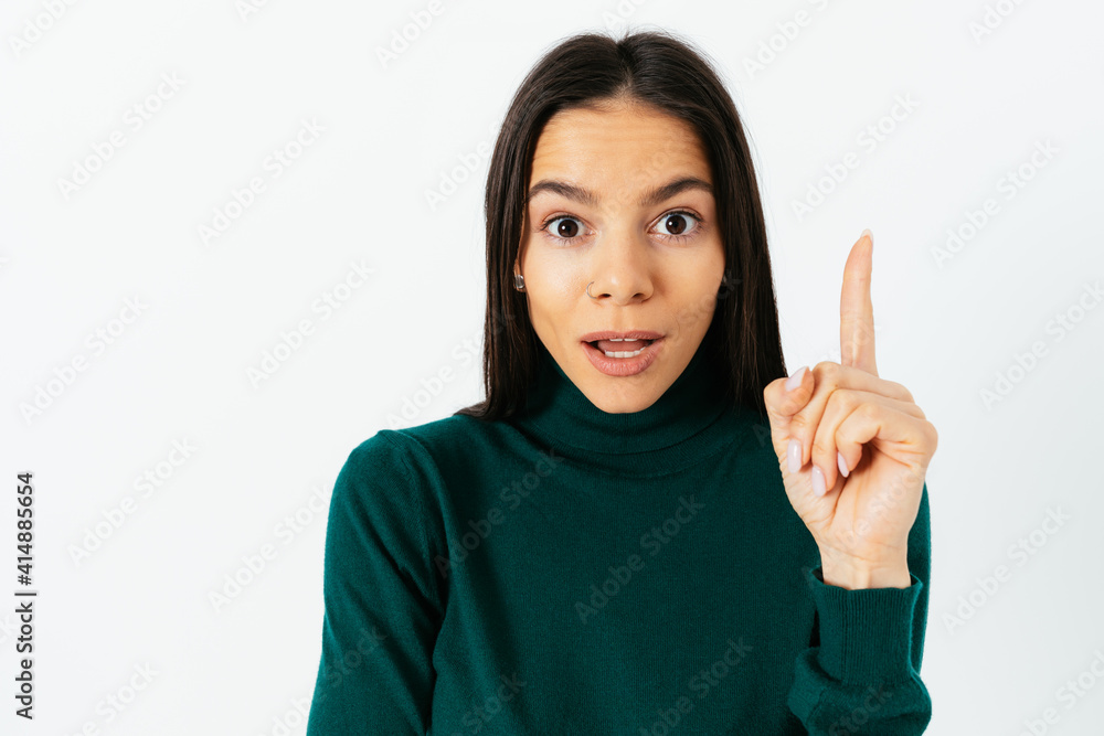 Portrait brunette woman pointing with one index finger up and looking at camera Portrait brunette woman pointing with one index finger up and looking at camera