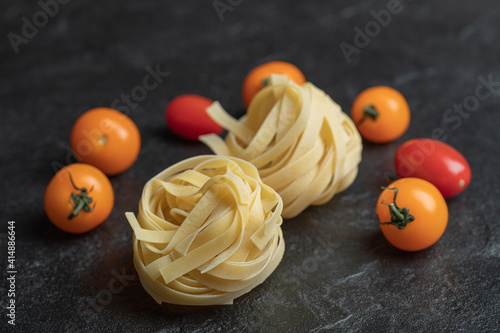 Uncooked nest pasta with cherry tomatoes on a dark background