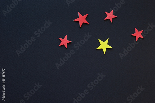 Four red paper stars and single yellow star on dark background; 5 star color design; flag type; top view, flat lay