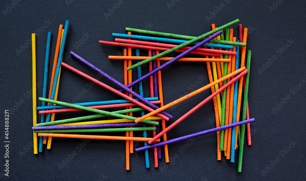 Colorful wooden sticks randomly scattered on black background; stack of colorful wooden sticks; multicolored shape; top view, flat lay
