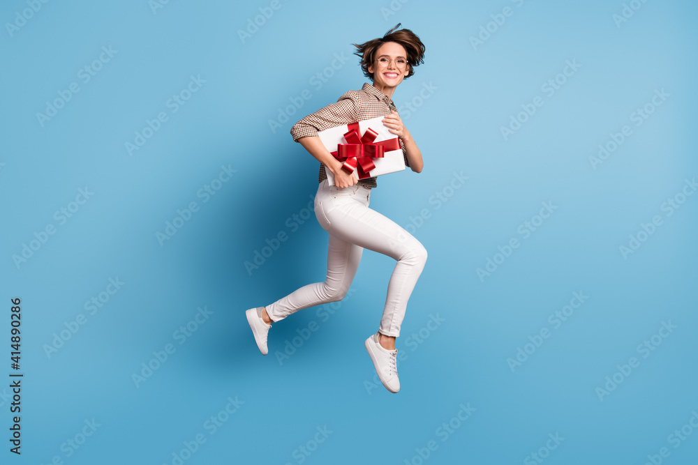 Fototapeta premium Full body profile portrait of cheerful girl hold giftbox jump running toothy smile isolated on blue color background