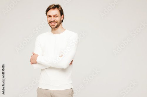 Portrait of handsome smiling hipster lumbersexual businessman model wearing casual white sweater and trousers. Fashion stylish man posing against gray background in studio © halayalex
