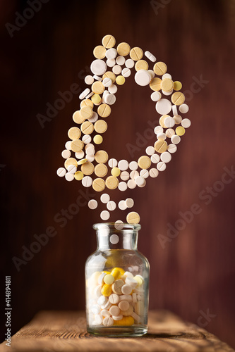 various pills fly out of a glass jar in the form of letter D on a wooden background photo