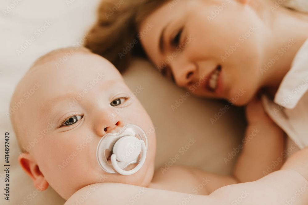 Happy mom hugs and kisses her little child on the bed at home Happy mom hugs and kisses her little child on the bed at home