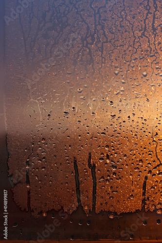 Vertical natural background with water drops on a window with sun rays, condensation on glass with dripping drops